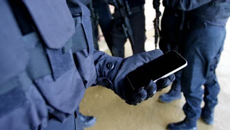 Close-up-of-military-soldier-holding-mobile-phone-at-military-base-4k