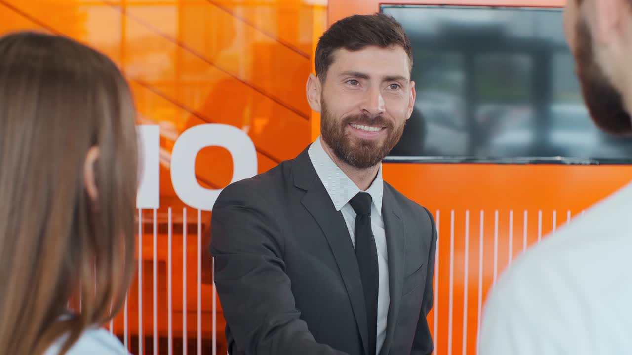 vendedor transmitiendo llaves a una joven pareja en un concesionario de automóviles.