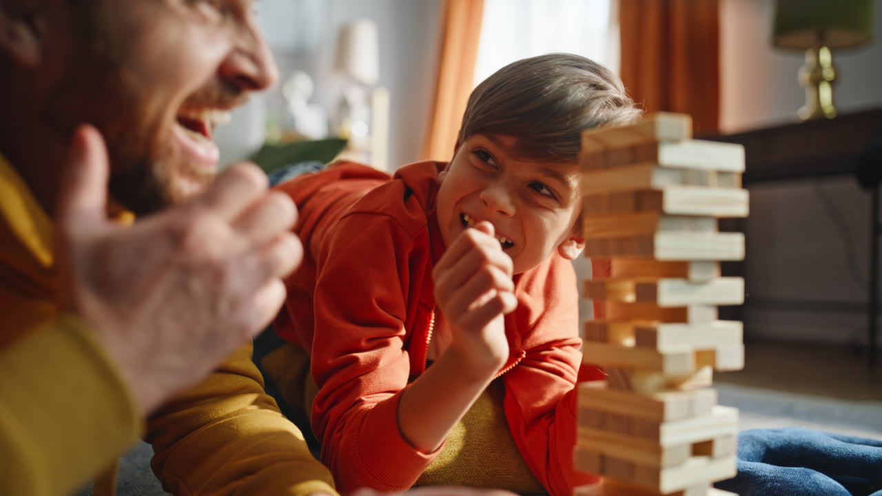 Primo piano di padre e figlio che giocano a un gioco da tavolo, ridendo e trascorrendo il tempo libero in famiglia, sdraiati sul pavimento.