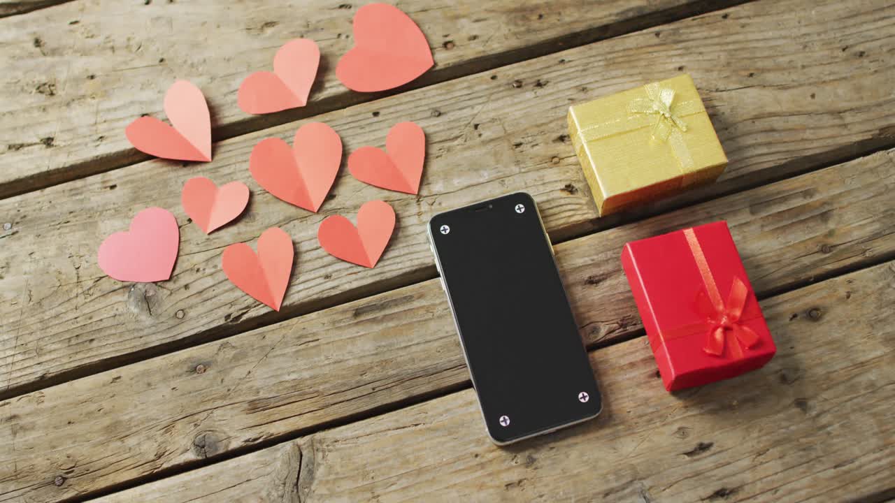 Paper hearts and smartphone with gifts on wooden background at valentine's day
