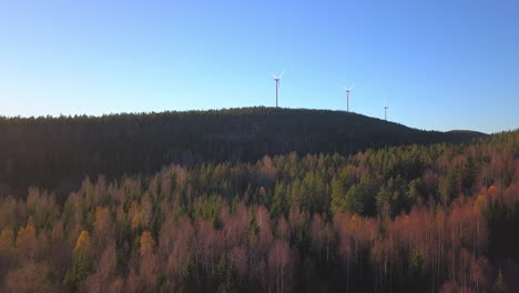 aerial drone view over leafless trees and a hill, heading towards a wind power generator turbine, on the top of a mountain, in hoga kusten, vasternorrland, sweden