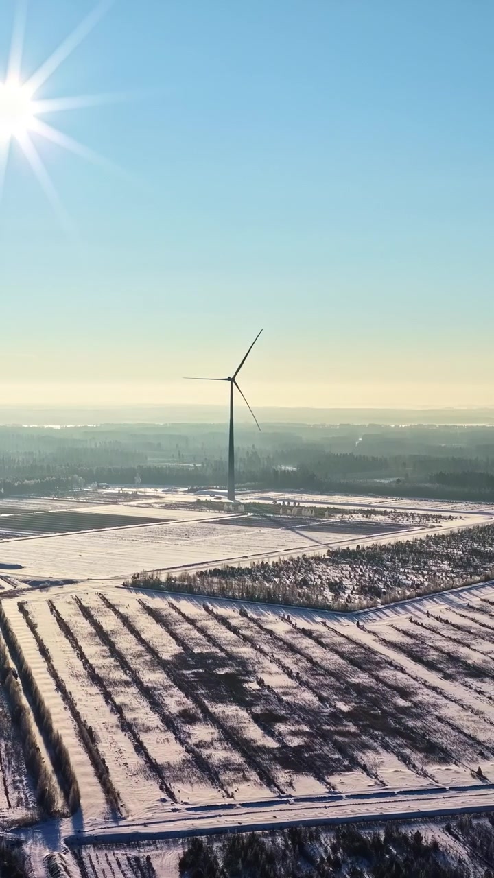 Windräder ragen hoch über schneebestäubten Feldern unter einem klaren Morgenhimmel auf. Ideal für Themen der erneuerbaren Energien oder Winterlandschaftsprojekte.