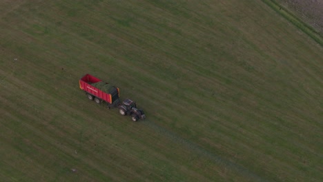 Tractor-is-collection-fresh-grass-from-the-land-during-sunset,-aerial