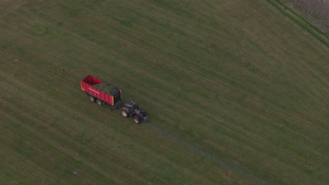 tractor is collection fresh grass from the land during sunset, aerial