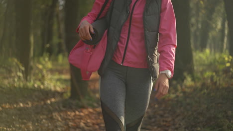person walking in a forest with a yoga mat and sports bag