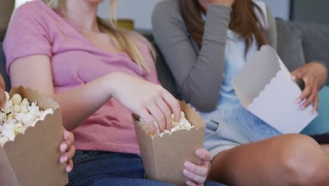 diverse teenager girls friends eating popcorn and watching tv at home, slow motion