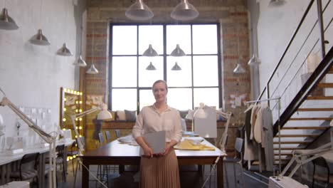 Zoom-In-Of-Female-Fashion-Designer-Holding-A-Notebook-And-Posing-For-Camera-In-Sewing-Workshop