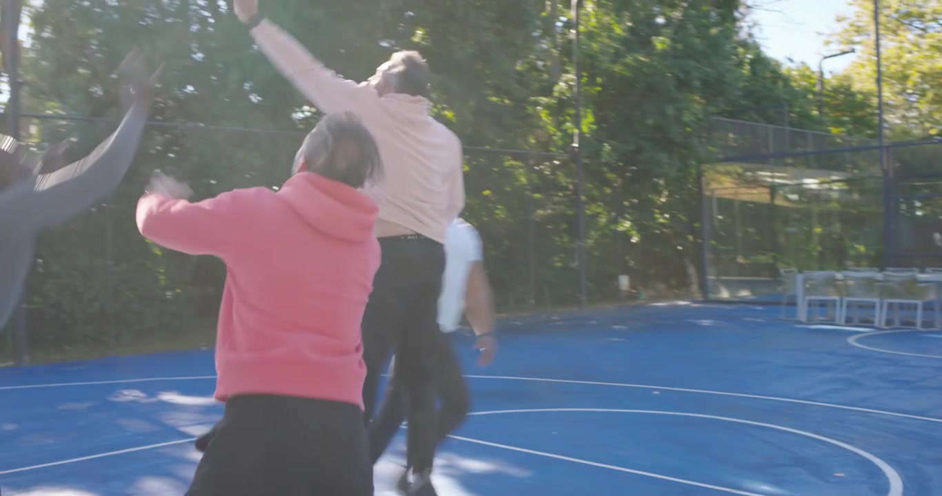 Hombres diversos reaccionando a un jugador de camiseta blanca que sostiene un balón naranja, regateando y disputando en una cancha azul para anotar.