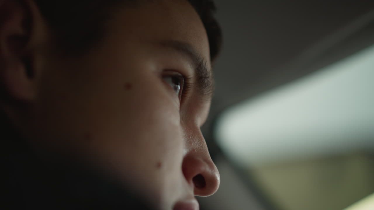 Lower view of commuter looking around windshield while driving through busy street with blurred traffic outside, highlighting attentive gaze and urban motion in natural daylight and cityscape details