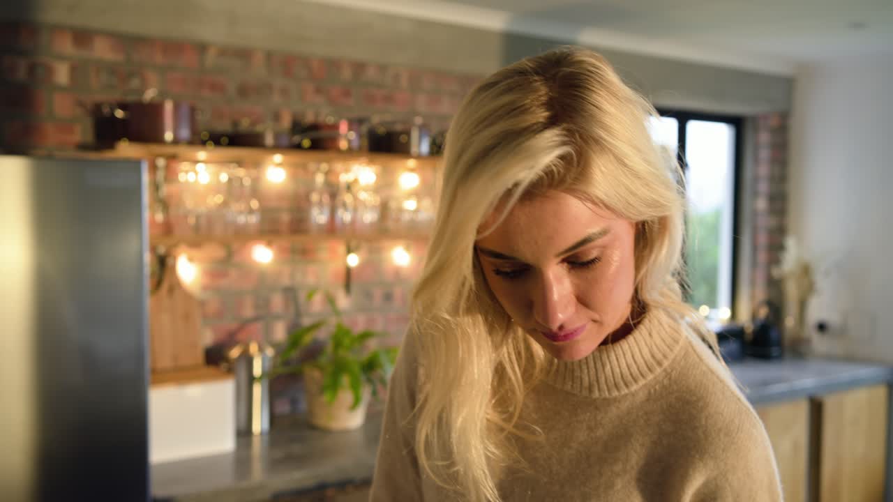 Woman at home kitchen counter picking up red mug, inhaling aroma then sipping slowly and smiling