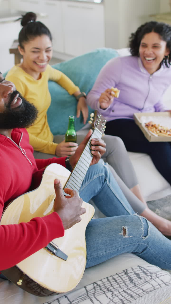 Vertical video of happy, diverse female and male friends playing guitar and laughing, slow motion