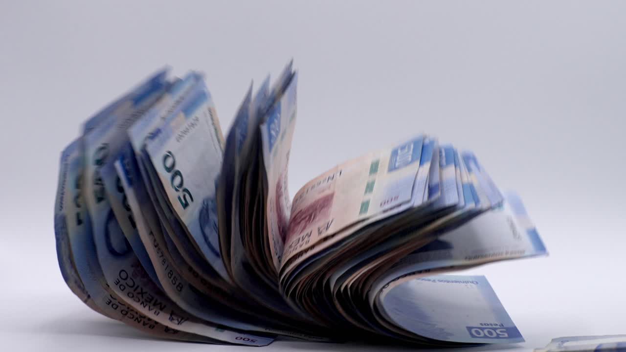 Bundle of Mexican pesos falling under studio lighting. Close up