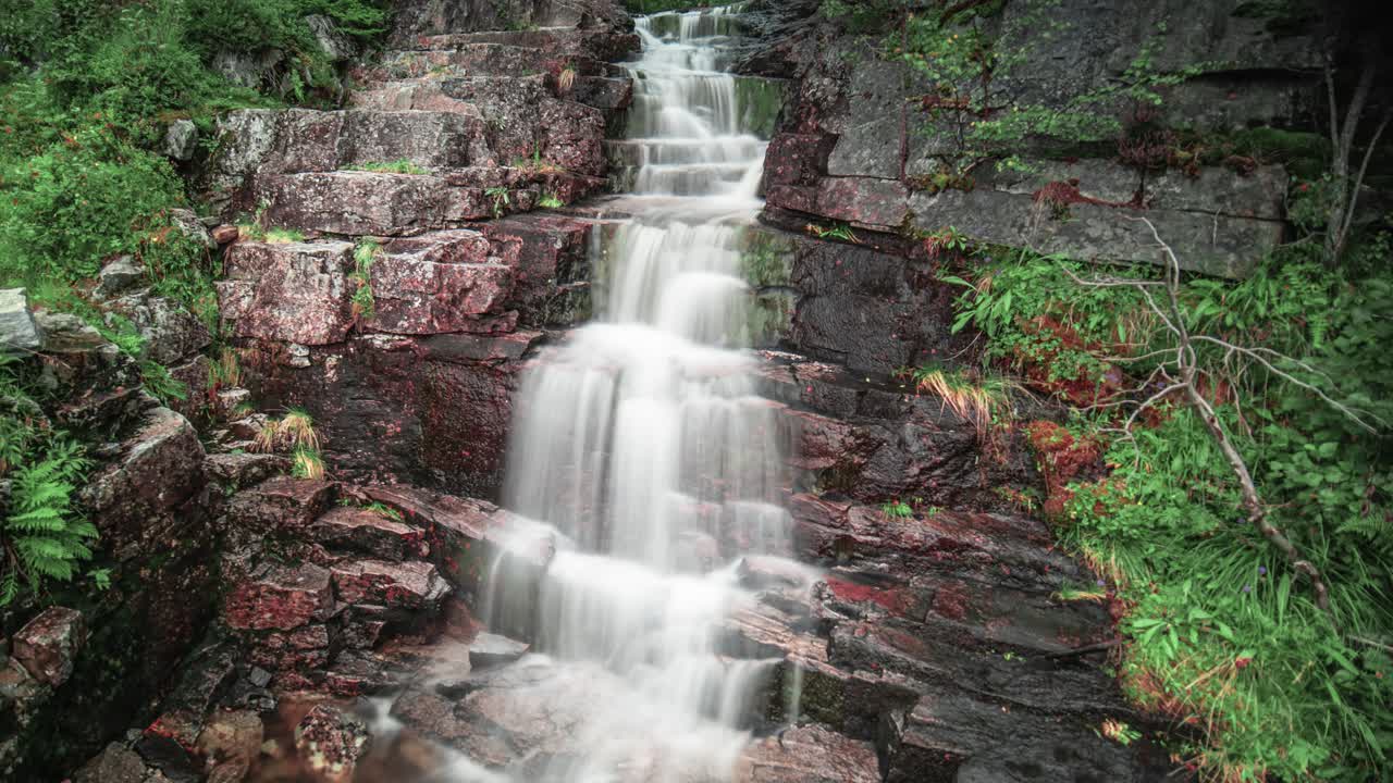 una cascada rodeada de vegetación en el bosque cae sobre piedras oscuras