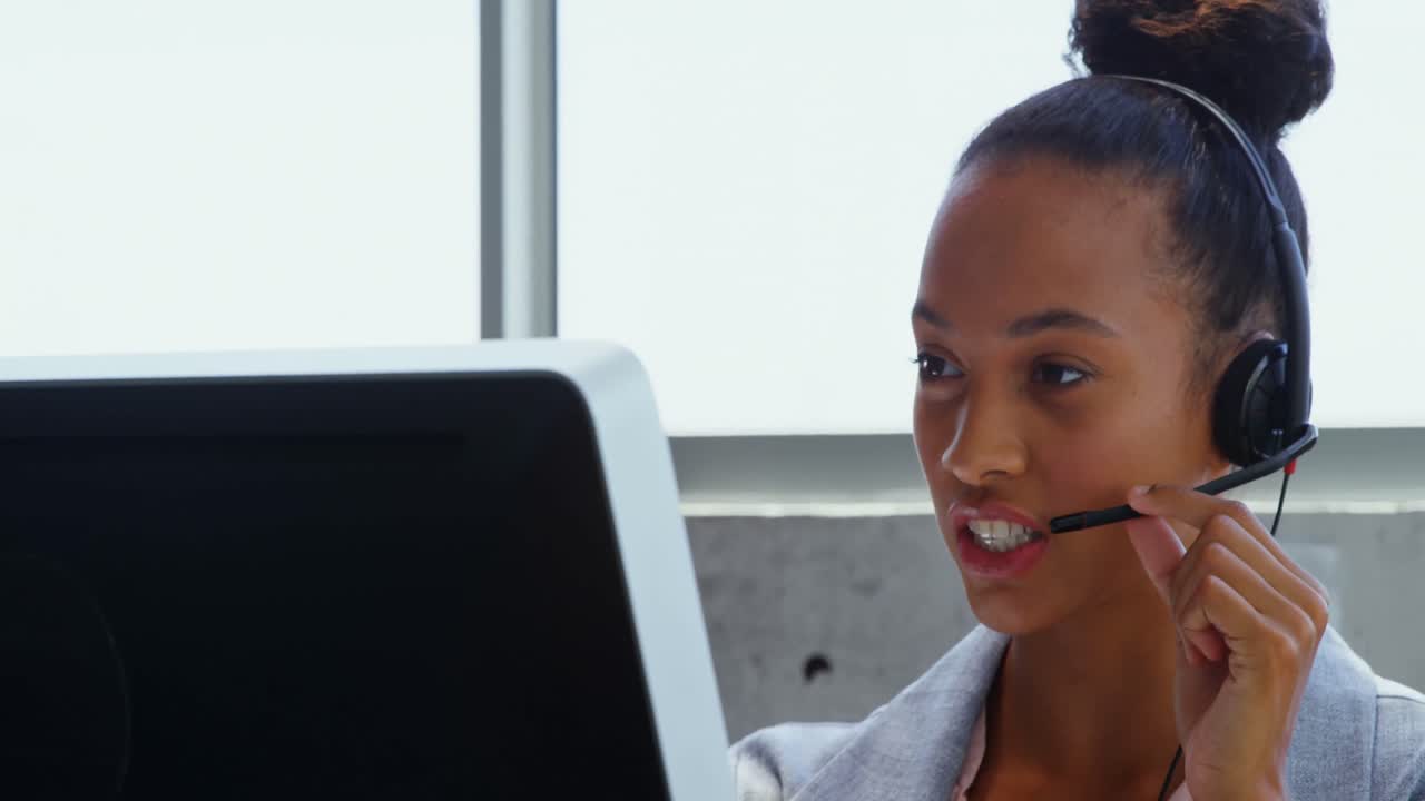 Vista frontale di una donna d'affari afroamericana che parla con le cuffie alla scrivania in un ufficio moderno 4k