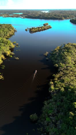 vertical: drone closes in on boat on juma river in the amazon, surrounded by jungle