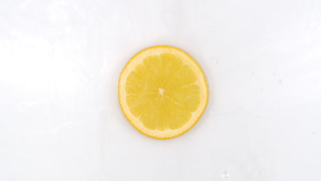 On-a-white-background-a-splash-of-water-falls-on-a-slice-of-lemon-in-slow-motion.