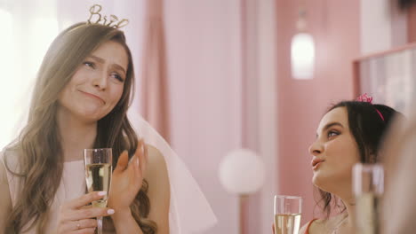 close up view of bachelor girl with headdress holding champagne crystal glasses and talking with her friends