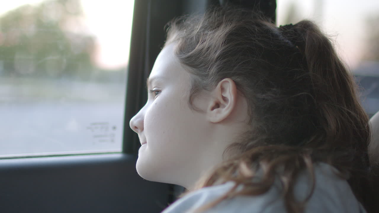 A young girl riding in a car gazes out the window on a breezy sunny day