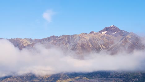 mountain peaks rise above drifting fog under a clear blue sky in queenstown, new zealand. captured in serene natural lighting