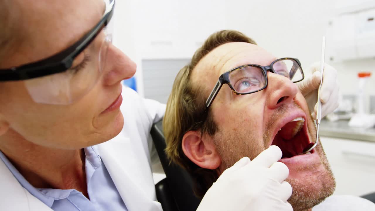 Paziente maschio d'esame del dentista femminile con gli strumenti