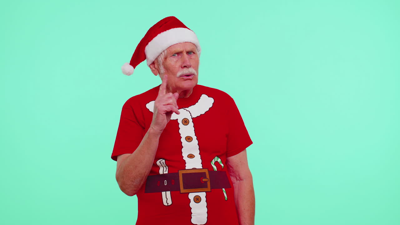 크리스마스 티셔츠를 입은 은이가 손가락을 입술에 러 침을 지시하고 신호, 비밀을 나타니다.