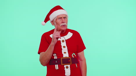 senior old man in christmas t-shirt presses index finger to lips makes silence gesture sign, secret