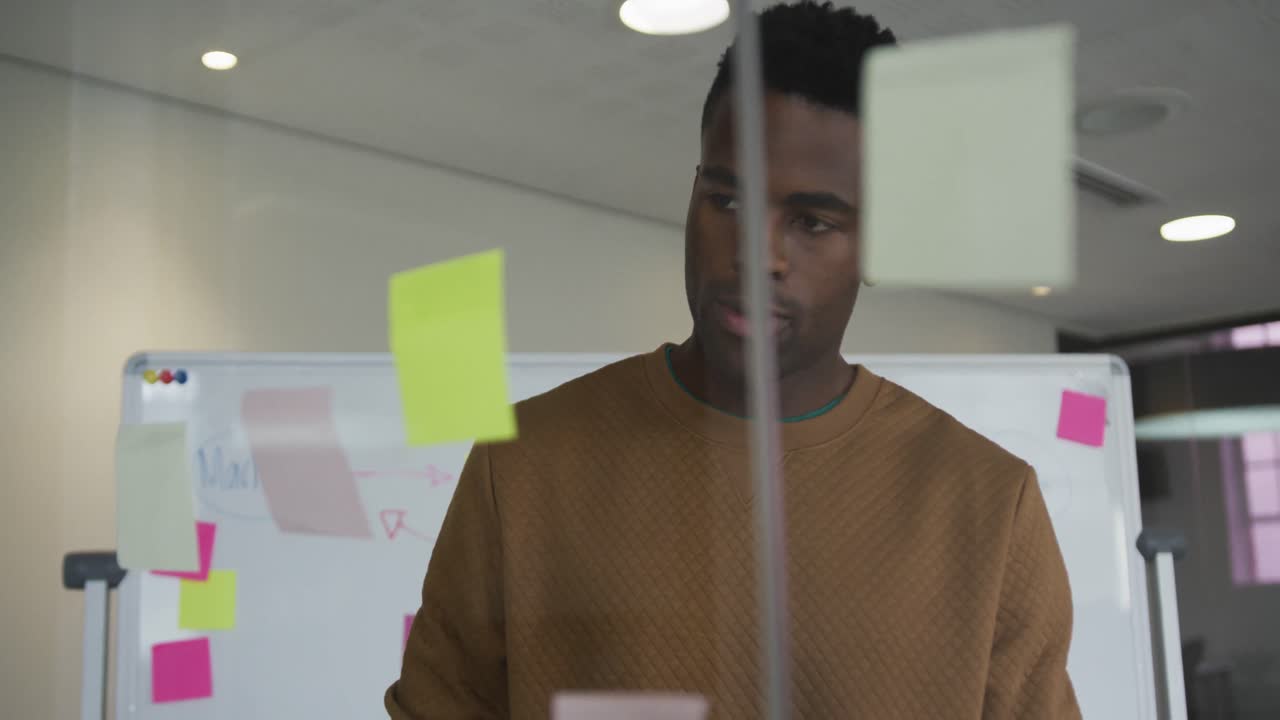 African american businessman standing behind glass wall with sticky notes and pondering