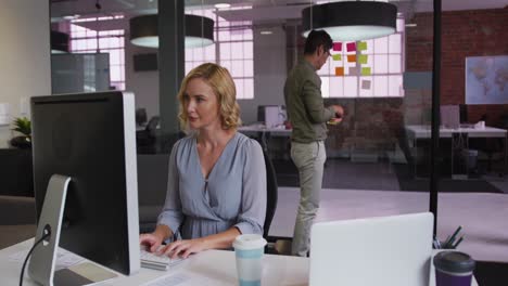 Caucasian-businesswoman-working-on-laptop-with-mixed-race-colleague-in-background-using-memo-notes