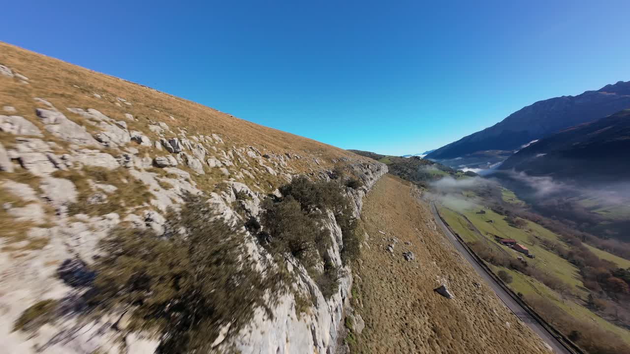 FPV drone follows the mountain ridge then performs a dramatic dive, revealing a vast misty valley bathed in sunlight.