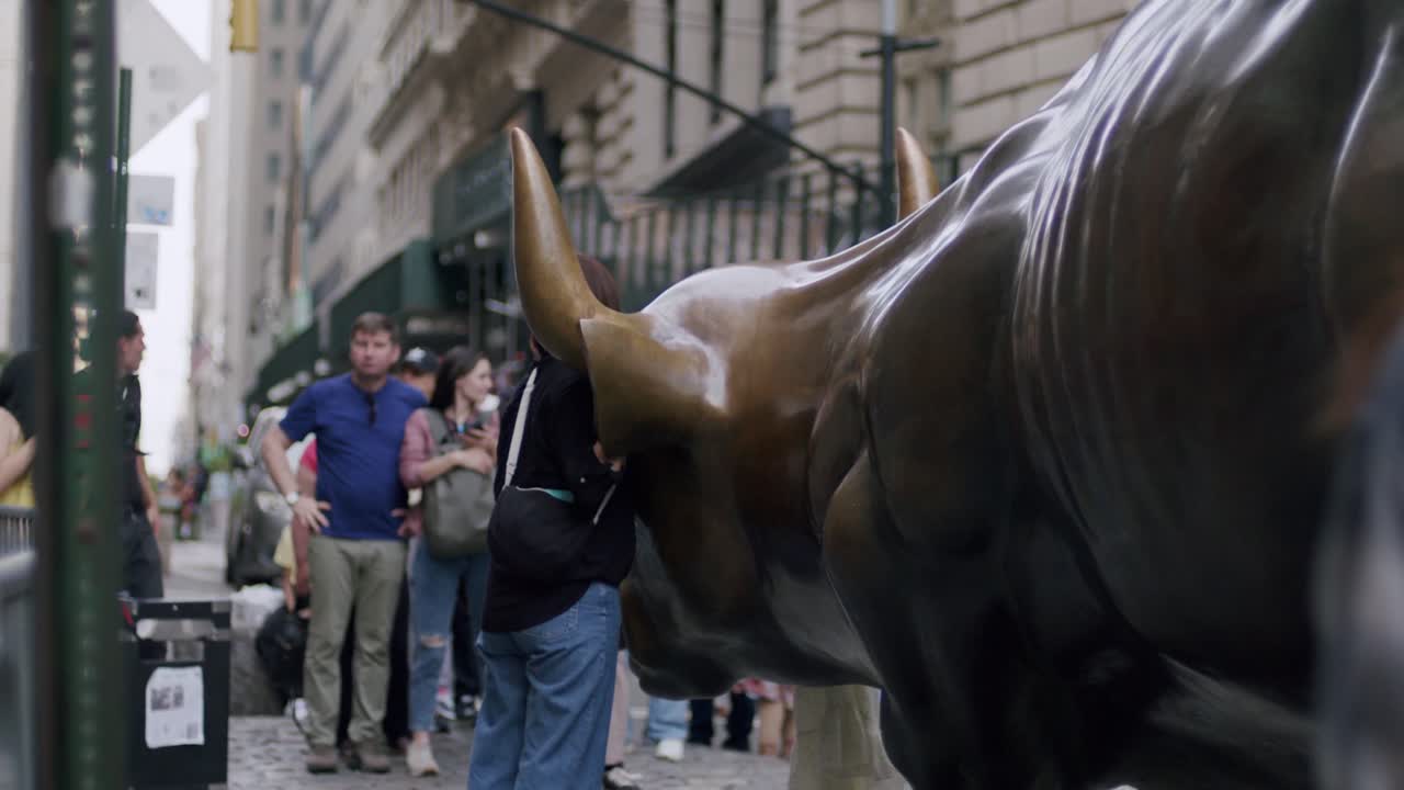 Tourists gather near the Charging Bull statue in New York City, with someone taking a selfie