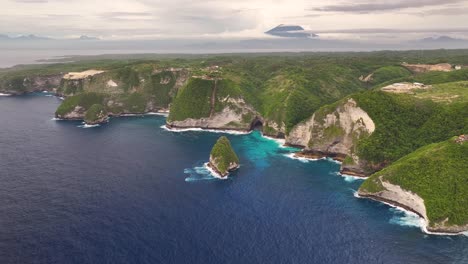amazing cliff formations on nusa penida, bali coastal. volcano on horizon. drone panoramic,