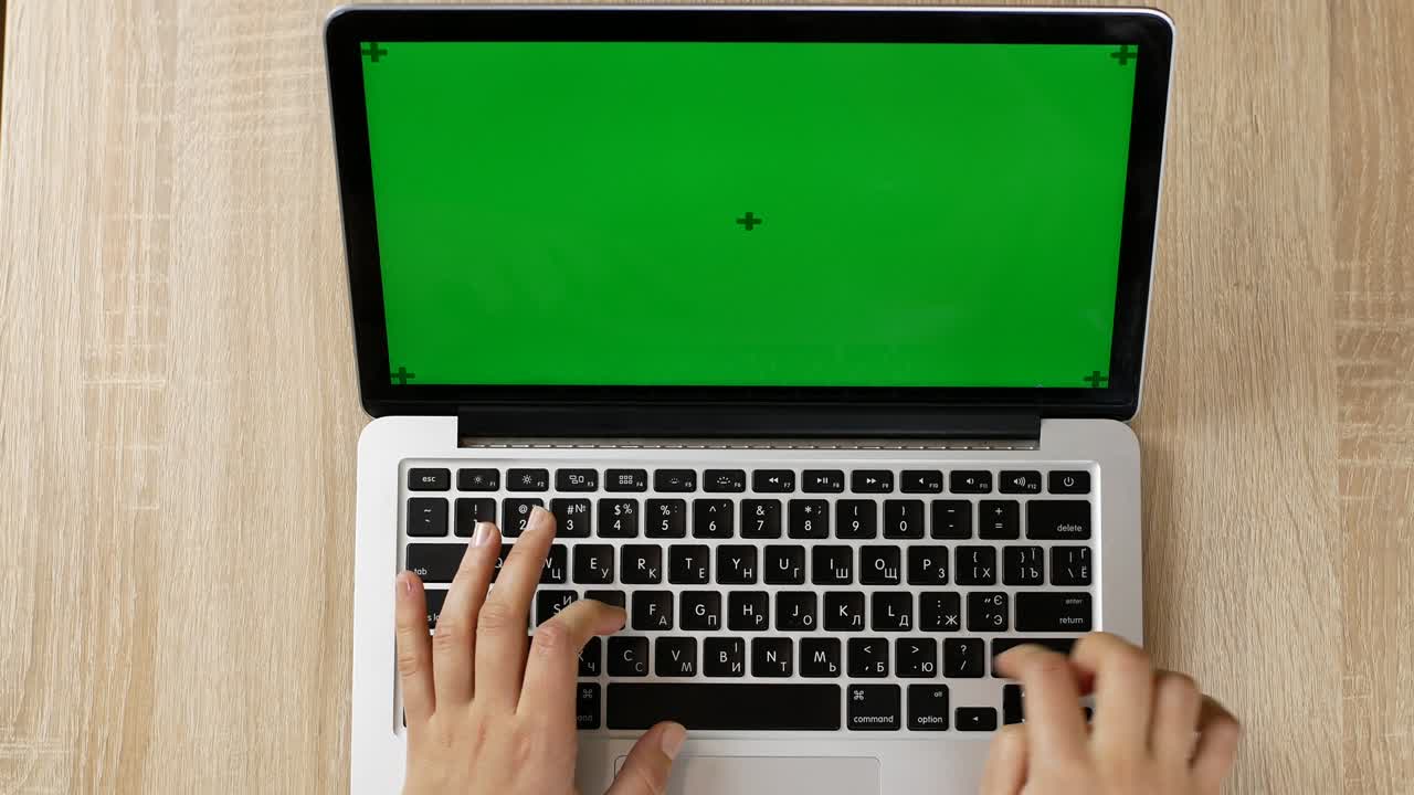 A woman is typing on a laptop with green screen sitting on the working place in