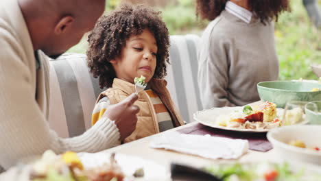 a young boy eats broccoli with his dad at the dinner table.