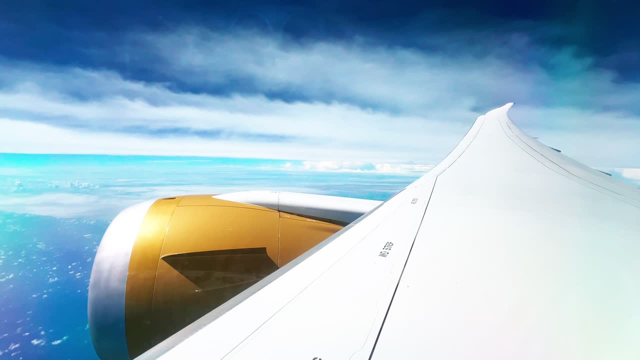 Scenic view from airplane window showing white wing, golden engine, and turquoise ocean below with dramatic sky — perfect for travel, aviation, and tourism projects