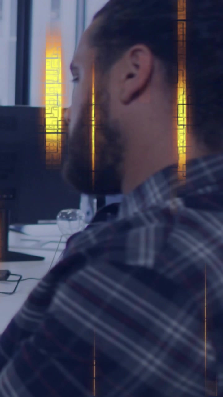 Vertical video: Bearded man sitting desk glancing screen and causing gold overlay showing tech data