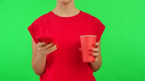 woman holding phone and drink in front of green screen