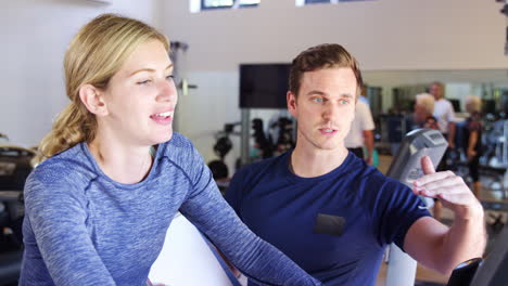 woman exercising on cycling machine being encouraged by personal trainer in gym