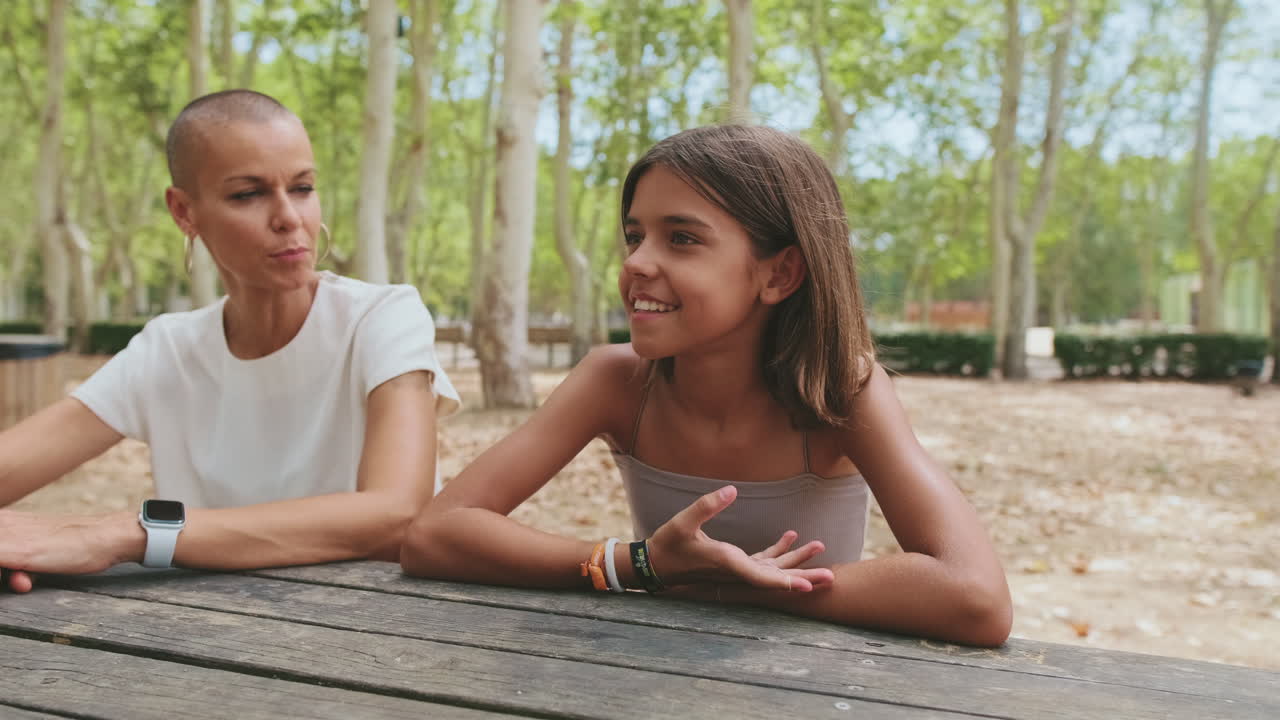 Menina e Mulher Sorrindo Conversando em uma Mesa de Piquenique em um Parque