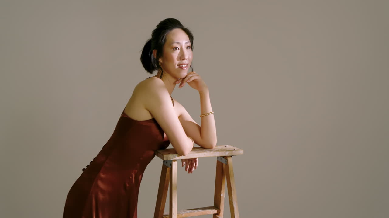 Slanted light patches guiding Asian female model leaning on wooden stepladder and posing in studio