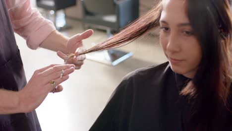 midsection of caucasian male hairdresser cutting ends of female client's hair at salon, slow motion