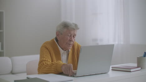 senior woman with laptop computer calling on smartphone at home. old woman having a video call on the laptop smiling and talking happily indoors in a cozy apartment. doctor video calling older patient