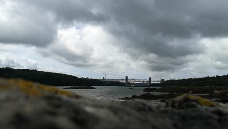 Blick-über-Den-Unscharfen-Felsvordergrund-Zur-Bewölkten-Menai-Straße,-Britannia-Brücke-Und-Anglesey