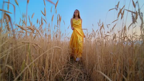 woman in a yellow dress walking through a wheat field at sunset