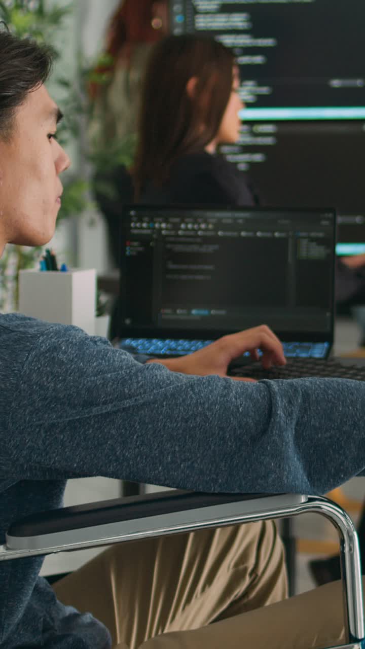 Vertical video: Focused software developer in wheelchair writing server code in agency data room
