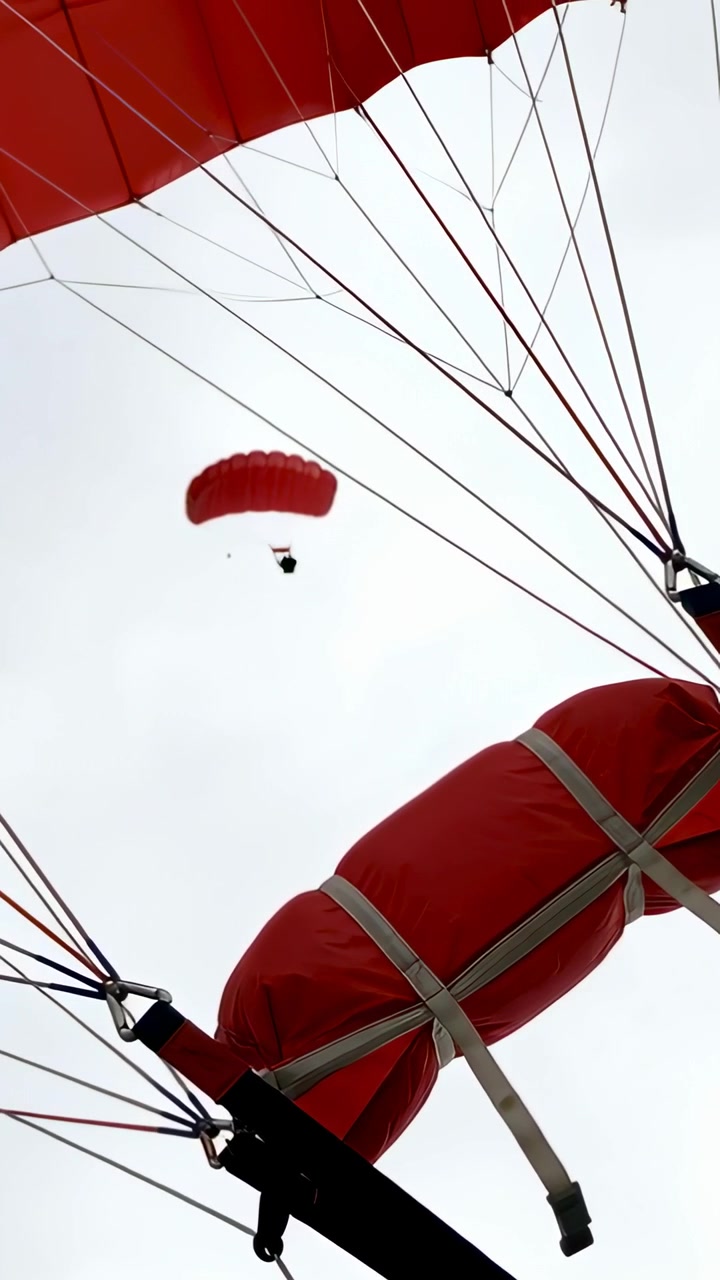 Video verticale: Apertura del paracadute principale, si vede un paracadutista lontano che cade sotto una vela rossa tra le nuvole con una borsa.