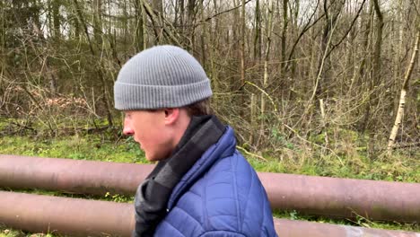 slow motion shot of thoughtful young man with hat walking along rural forest path during autumn with leafless trees in background