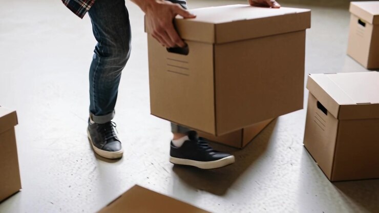 Stepping, man in jeans and flannel gripping and lifting box, organizing storage on concrete floor
