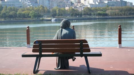 woman in hijab sitting on a bench by a lake