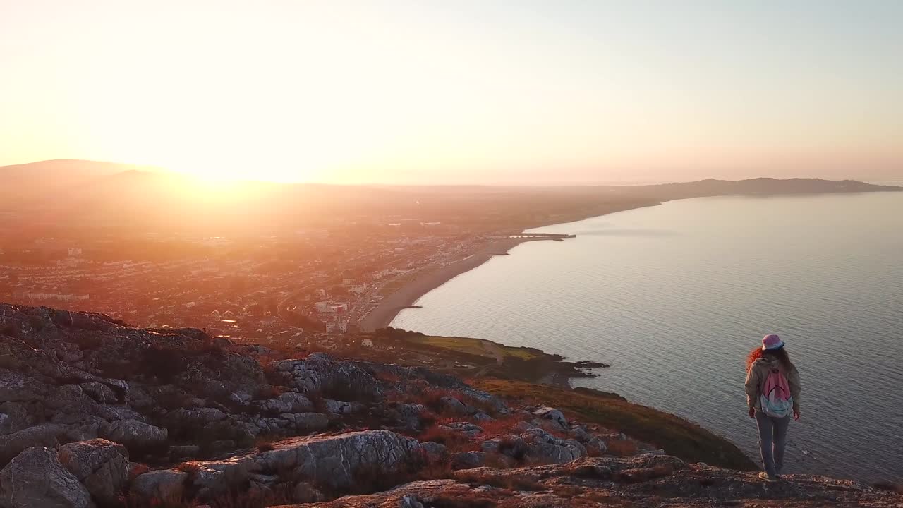 Vista aérea de mulher caminhante com mochila em penhasco acima do mar e paisagem urbana de Bray na Irlanda.