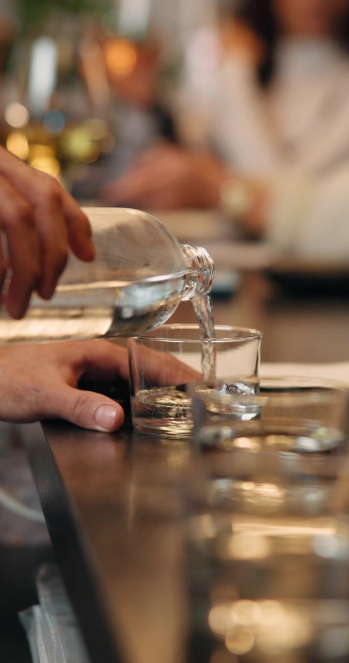 Hånd hælder vand fra glasflaske i glas på restaurant